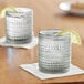 Two Fortessa smoke gray double old fashioned glasses filled with ice and lemon on a white napkin.