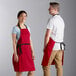 A man and woman wearing Choice red aprons standing next to each other on a counter in a professional kitchen.