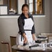 A woman in a white apron setting a table.