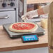 A person measuring a pizza on an AvaWeigh pizza scale.