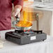 A person cooking food in a pan on a Choice portable gas stove.