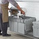 A person in an apron putting food into a Choice stackable chafer tote.