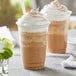 A close-up of a Capora spiced chai latte with whipped cream and a straw.