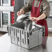 A man in a red apron putting a grey Choice chafer lid in a grey tote box with attached lid.