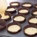 A tray of cupcakes with yellow batter being poured into Mini Glassine cupcake liners.