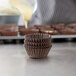 A person pouring chocolate into a stack of brown Mini Glassine Baking Cups.