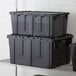 A stack of black Choice stackable chafer totes on a shelf.