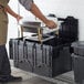 A person holding a metal container with food in a black Choice stackable storage box.