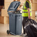 A woman in a safety vest using a Lavex step-on attachment to put a black plastic bag into a trash can.