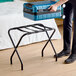 A black folding luggage rack with nylon straps, designed for holding suitcases.