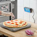 A person using an AvaWeigh pizza scale to cut a pizza on a counter.