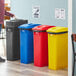 A woman standing next to a Lavex 4-stream rectangular recycle station with black, blue, red, and yellow bins.