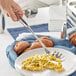 A hand holding a Choice stainless steel pasta fork over a bowl of pasta.