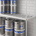 A white Regency bottom shelf holding a group of kegs with blue containers on it.