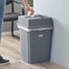 A woman using a paper towel to clean a Lavex gray square trash can.