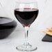 A Libbey red wine glass filled with red wine on a table in a winery cellar.