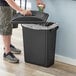 A man putting a coffee cup into a black Lavex rectangular trash can.