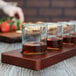 Anchor Hocking sample glasses filled with brown liquid on a wooden board.