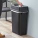 A woman putting a tissue in a black Lavex trash can.