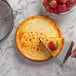 A person cutting a cheesecake with a slice of strawberry on top using a Choice non-stick springform cake pan.