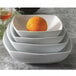 A stack of square white Princesquare bowls with an orange in one of them.