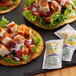 Three tacos with Salsa Del Sol sauce packets on a table.