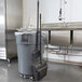 A Rubbermaid upright dustpan hanger in a kitchen with a broom and trash can.