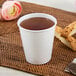 A Dart ThermoGuard white paper hot cup full of brown liquid on a table next to a pink flower.