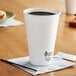 A white Dart ThermoGuard paper hot cup with a lid on a table with a cup of coffee.