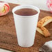 A Dart ThermoGuard white paper hot cup filled with tea on a table next to a flower.