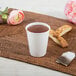 A Dart ThermoGuard white paper hot cup with tea and a tea bag on a table.