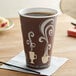 A brown Dart paper hot cup with white steam print designs filled with coffee on a table.