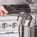 A hand holding an American Metalcraft stainless steel measuring cup with chocolate chips.