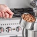 A person using an American Metalcraft stainless steel measuring cup to measure nuts.