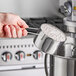 A hand using an American Metalcraft stainless steel measuring cup to scoop flour.