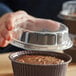 A person holding a Novacart clear plastic dome lid over a cupcake.