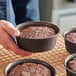 A person holding a brown paper baking mold filled with chocolate cake.