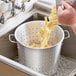 A hand pouring pasta noodles into a Choice aluminum vegetable colander.