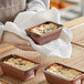 A person holding a tray of small brown paper loaves.