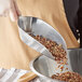 A hand using a Choice aluminum scoop to pour nuts into a bowl.