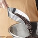A hand using a Choice aluminum flat bottom scoop to pour chocolate chips into a bowl.