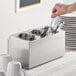 A hand holding a fork and knife in a stainless steel flatware organizer.