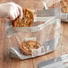 A gloved hand holding a large "Fresh Bakery" cookie in a plastic bag.