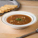 A Fineline Silver Splendor plastic soup bowl filled with soup next to crackers.