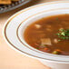 A Fineline Silver Splendor plastic soup bowl with ivory and gold rim filled with soup and vegetables.