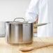 A silver Vollrath stainless steel sauce pan with a lid on a wooden surface with a wooden spoon next to it.