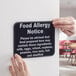 A person holding a black and white plastic "Food Allergy Notice" sign.
