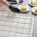 A person using a Choice stainless steel sheet cake marker to cut a cake.