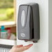 A person using a black Noble Chemical hand sanitizer dispenser.