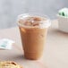 A clear plastic cup of coffee with a straw lid on a table with a muffin and cookie.